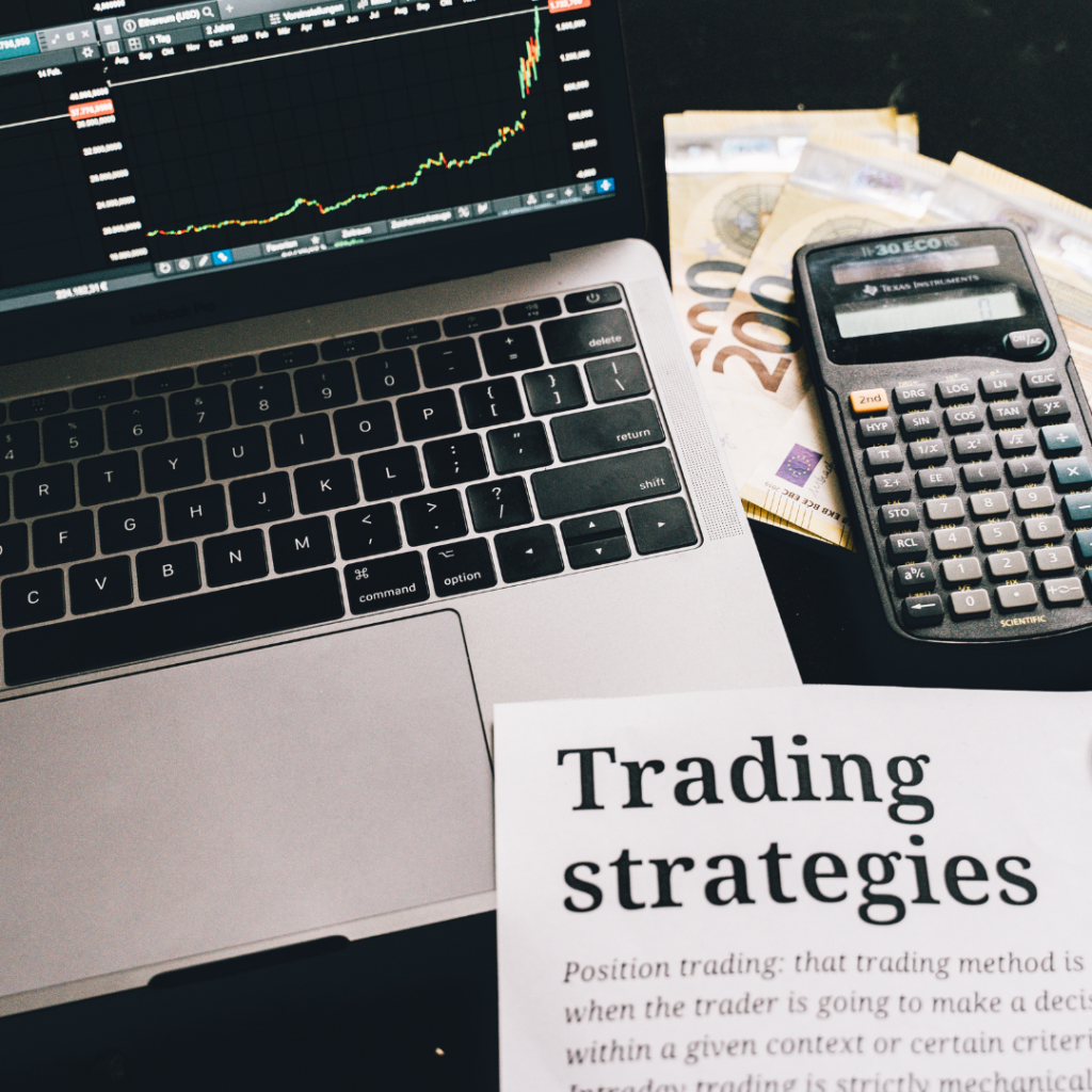 A close-up of a laptop displaying a trading chart, a calculator, Euro banknotes, and a printed page titled "Trading Strategies," symbolizing tools and methods for effective trading.